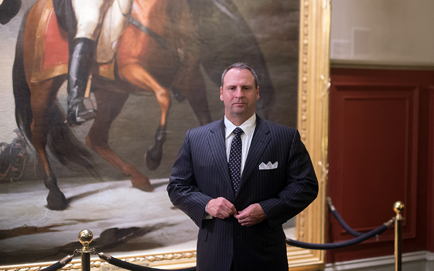 Man standing in a suit in front of a painting of a man riding a horse